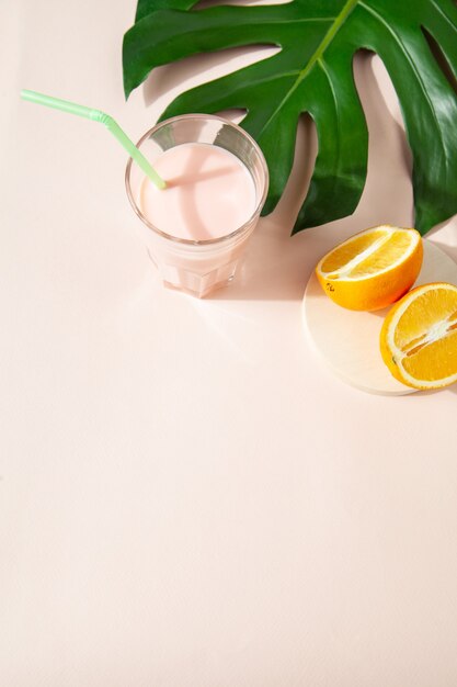 Angle élevé de smoothie frais et sucré en verre placé sur une table avec des moitiés de feuilles d'orange et de monstera en studio sur fond vert