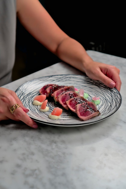 Angle vers le haut Caucasian Woman's Hands interagissant avec la fourchette et l'assiette de Tataki de thon rouge sur Ba blanc