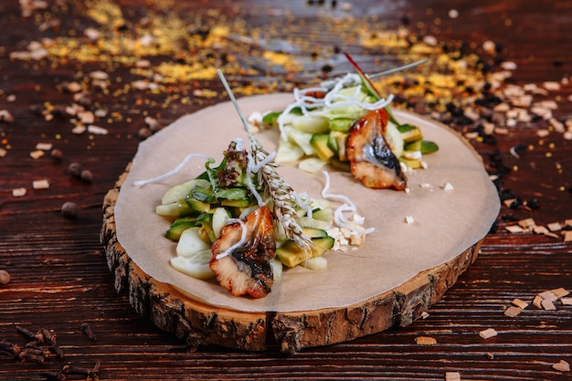 Anguille frite avec des légumes fraîchement coupés. Plat sur un support en bois