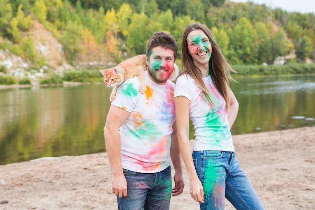 Animal de compagnie, tourisme d'été, festival holi et concept de nature - drôle homme et femme avec chat sur naturel