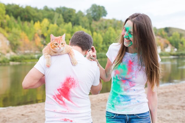 Animal de compagnie, tourisme d'été, festival holi et concept de nature - drôle homme et femme avec chat sur naturel