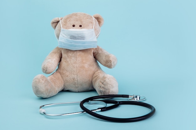 Animal ours en peluche en masque avec stéthoscope isolé sur bleu. Concept de soins de santé pour enfants