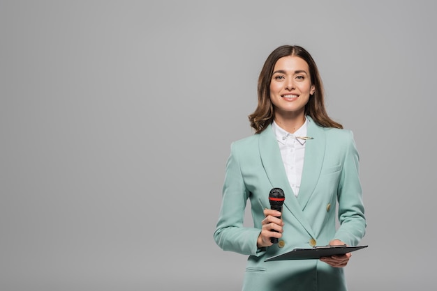 L'animateur d'événement insouciant et brunette en tenue formelle bleue tenant le microphone et le bloc-notes tout en regardant