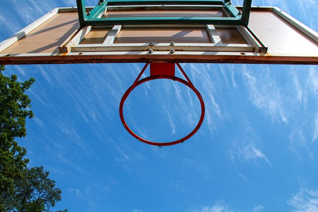 Anneau de basket-ball sur le fond un ciel bleu avec des nuages blancs et un arbre vert