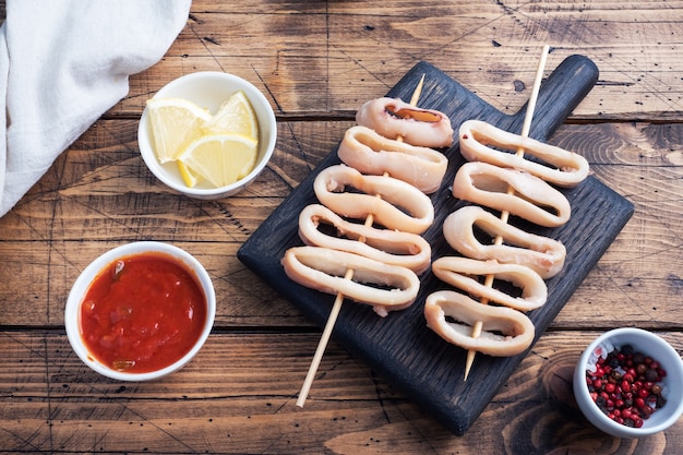 Anneaux de calamars frits sur une brochette avec sauce tomate et citron. Espace de copie de fond en bois foncé. Vue de dessus.