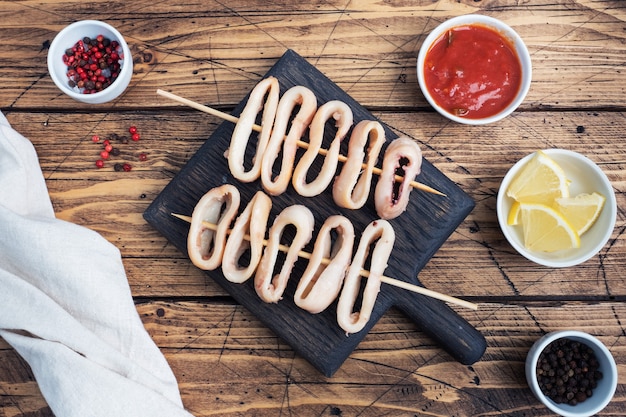 Anneaux de calamars frits sur une brochette avec sauce tomate et citron. Espace de copie de table en bois foncé. Vue de dessus.