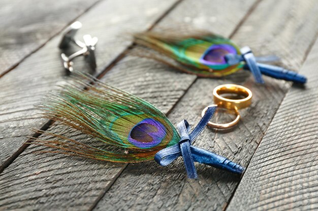 Anneaux de mariage boutons de manchette et boutonnières avec plume de paon sur table en bois