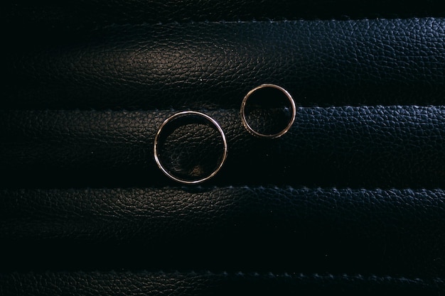 les anneaux de mariage des jeunes mariés se trouvent sur la chaise de barbier dans le salon de coiffure, fond sombre en cuir