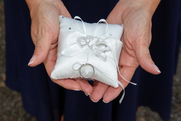 Anneaux de mariage de la mariée et du marié sur un coussin blanc dans les mains d'une femme témoin