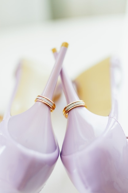 Anneaux d'or de mariage sur les talons des chaussures de mariée violettes