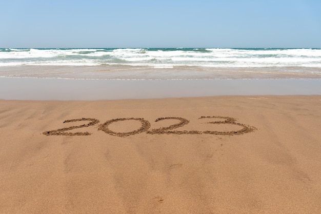 Année 2023 écrite dans le sable sur la plage avec la mer en arrière-plan