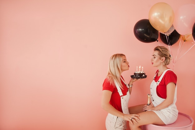 Anniversaire d'amitié. Deux filles soufflent des bougies. Copiez l'espace sur fond rouge corail.