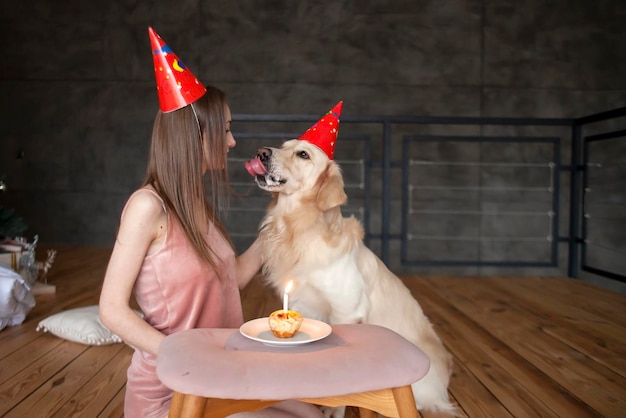 L'anniversaire du chien jeune femme avec golden retriever dans des chapeaux de fête célèbre son anniversaire