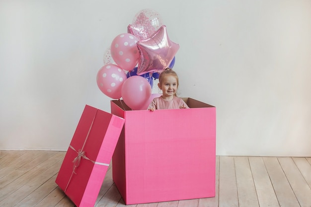 Anniversaire des enfants. Petite belle fille implantation dans une grande boîte cadeau rose avec des ballons