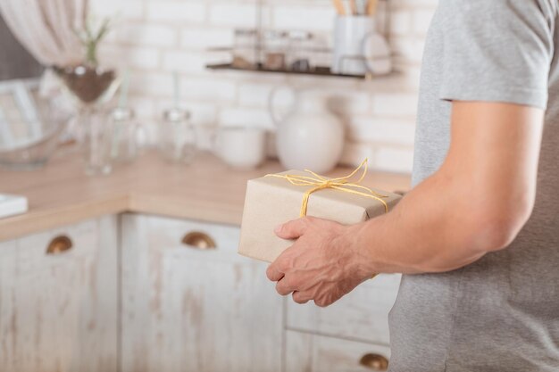 Anniversaire seul Photo recadrée d'un homme apportant une boîte cadeau faite main en papier rustique dans la cuisine Arrière-plan flou