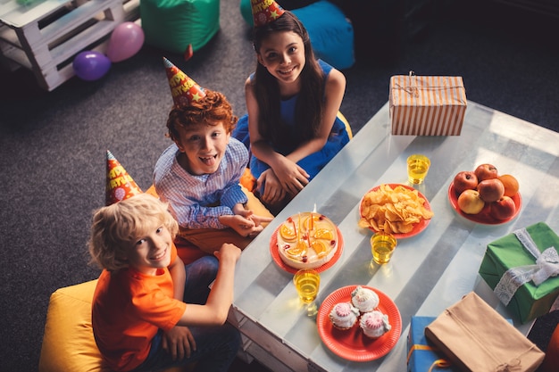 Anniversaire. Trois enfants assis à la table avec des aliments sucrés