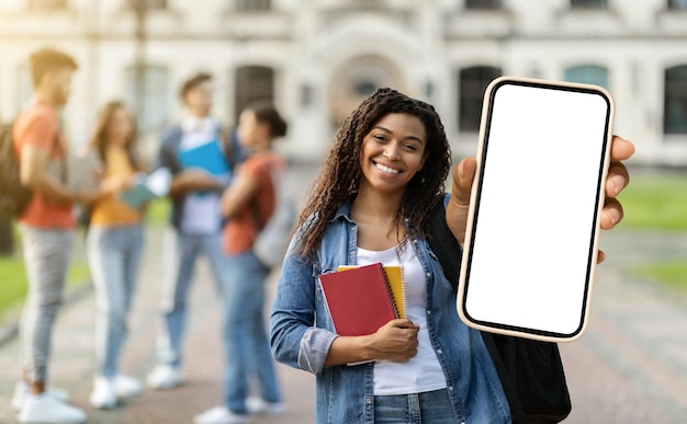 Annonce éducative étudiante noire souriante tenant un grand smartphone blanc à la main