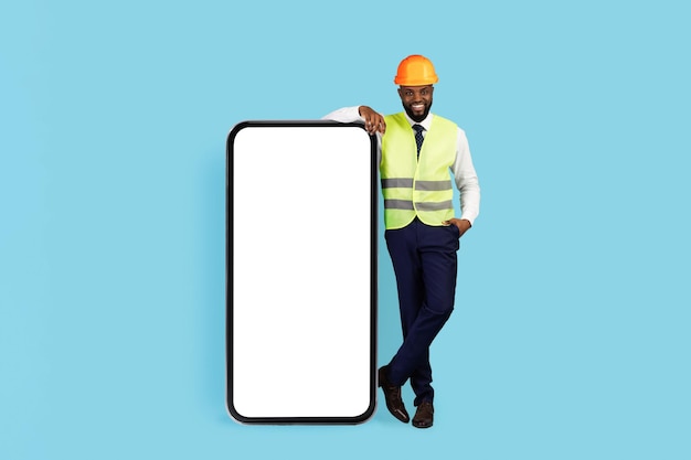 Annonce mobile bel ingénieur civil noir debout près d'un grand smartphone vierge