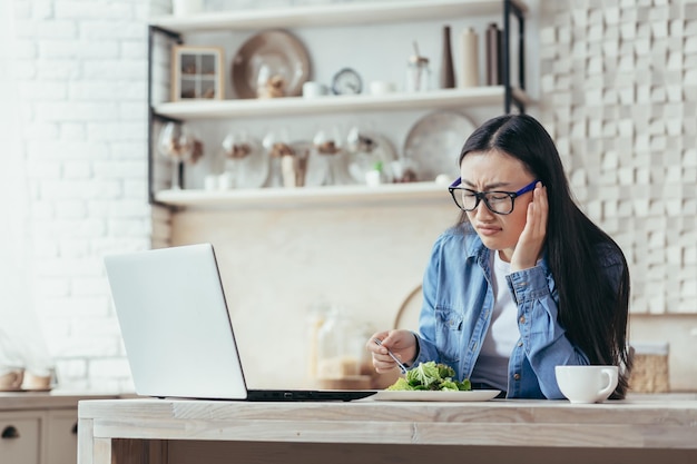 Anorexie insatisfaite et fatiguée jeune femme asiatique essayant de suivre un régime assis dans la cuisine avec un