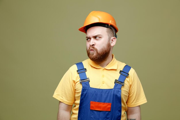 Anpluché regardant côté jeune constructeur homme en uniforme isolé sur fond vert