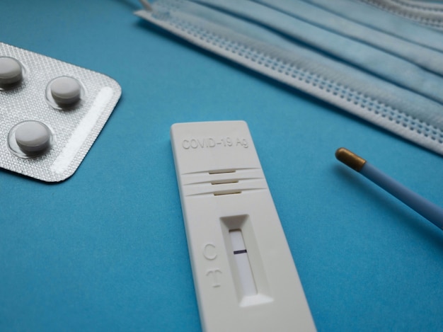 Antigentest Ð¡oronavirus 2019-nCoV avec un résultat négatif sur fond bleu clair à côté d'un thermomètre, d'un masque médical, de pilules et d'une seringue.