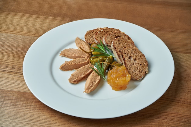 Antipasti appétissant - pâte d'oie avec de la confiture, du romarin et du pain de seigle en plaque blanche sur une table en bois /