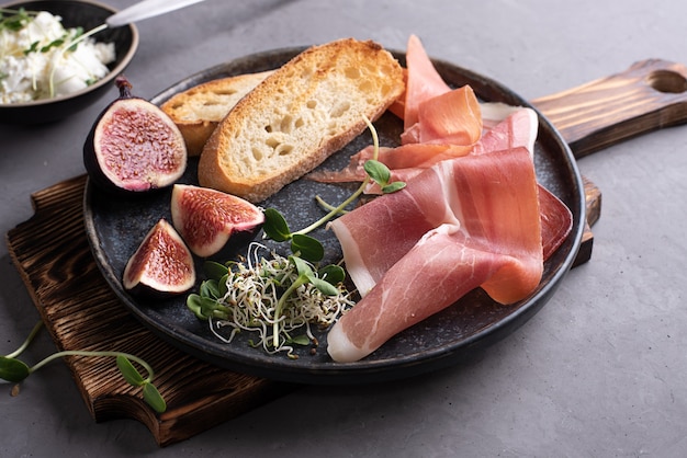 Antipasto italien de prosciutto, pain grillé, fromage à la crème sur une planche à découper sur fond gris, collation au jambon.