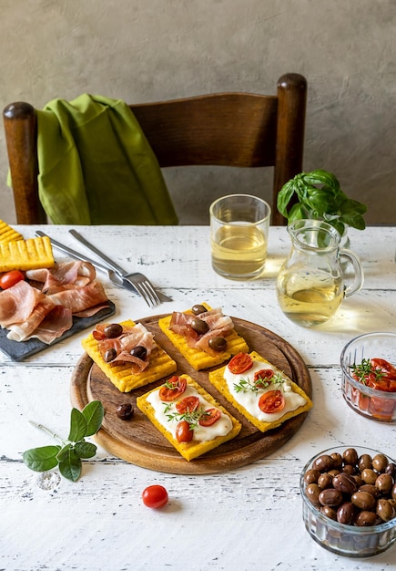 Antipasto avec polenta grillée garnie de fromage stracchino tomates herbes speck et olive