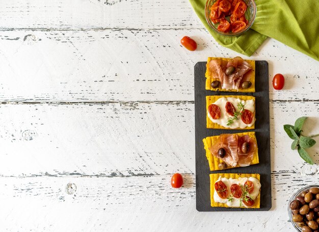 Antipasto avec polenta grillée garnie de fromage stracchino tomates herbes speck et olive