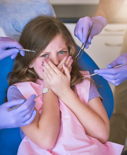 L'anxiété dentaire des enfants est très courante Photo d'une petite fille qui a l'air terrifiée alors que les dentistes se préparent à l'examiner