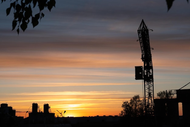 Aperçu du soir de la ville La silhouette de l'usine contre le ciel ou le coucher du soleil La grue à tour opère sur le territoire de l'usine