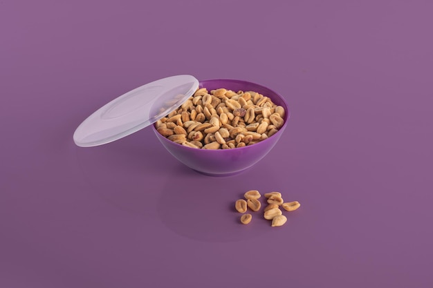 Apéritif d'arachides décortiquées dans un bol violet isolé sur fond violet