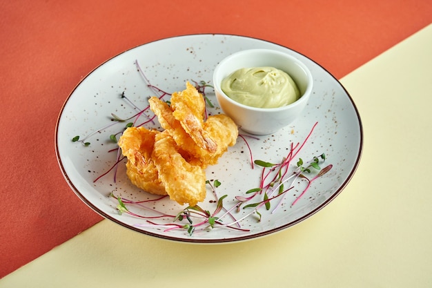 Apéritif - crevettes frites tempura avec sauce dans une assiette blanche sur une surface colorée. Finger food, pub