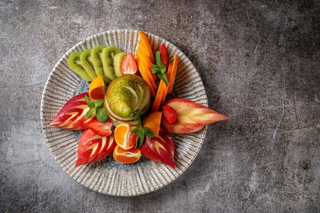 Un apéritif dans un restaurant, un assortiment de fruits. Fruits frais tranchés en couches sur une assiette à la menthe verte sur une table en pierre grise
