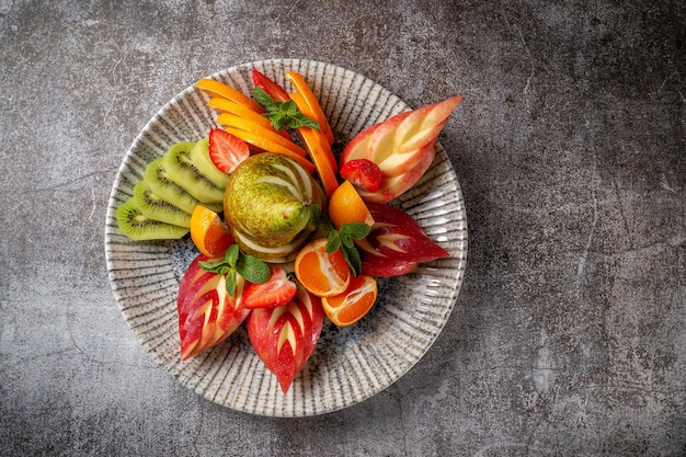 Un apéritif dans un restaurant, un assortiment de fruits. Fruits frais tranchés en couches sur une assiette à la menthe verte sur une table en pierre grise