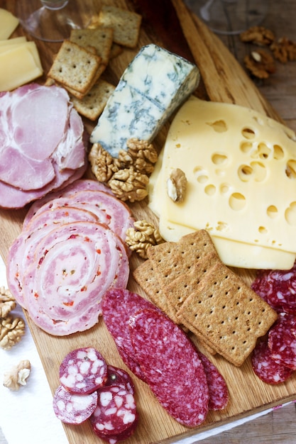 Apéritif de différents types de saucisses, viandes, fromages et craquelins sur une planche de bois, servi au vin.