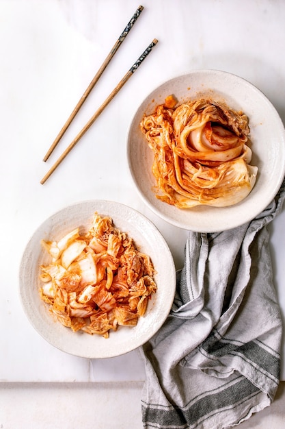 Apéritif fermenté traditionnel coréen fait maison chou kimchi entier et haché servi dans une assiette en céramique avec des baguettes sur un mur de marbre blanc. Mise à plat, espace