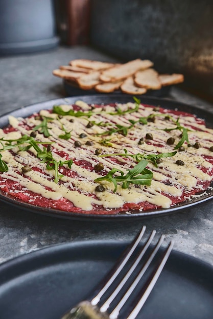 Apéritif froid de carpaccio de boeuf avec câpres de parmesan et roquette sur plaque noire mise au point sélective