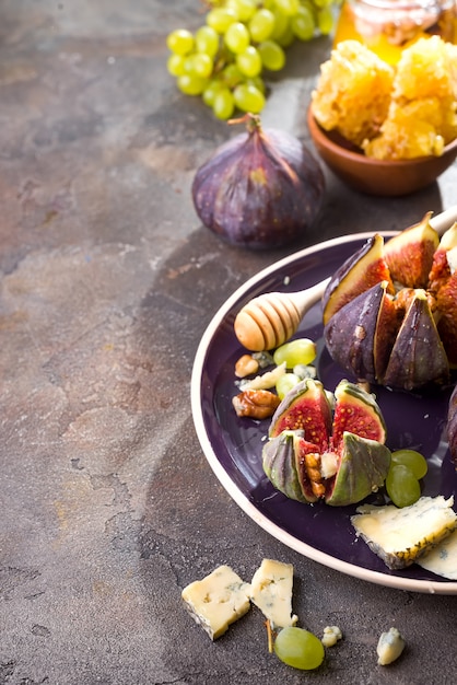 Apéritif gastronomique de figues au four avec fromage de chèvre, noix et miel sur une assiette en céramique