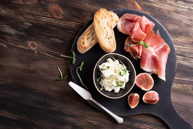 Apéritif italien, prosciutto aux fruits et fromage, jambon sec avec tranches de pain sur fond de bois sombre.