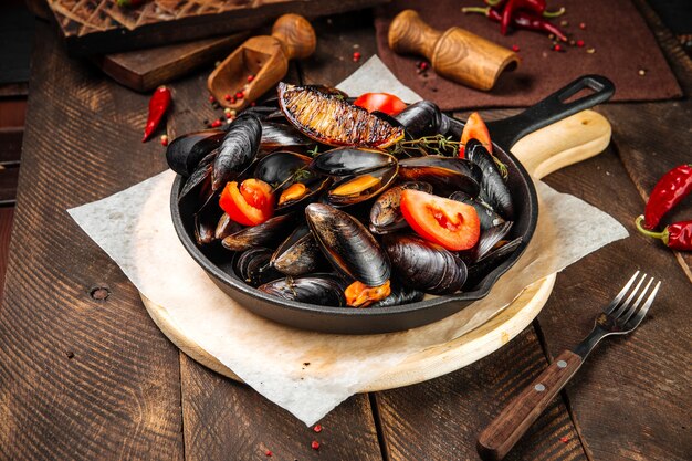 Apéritif de moules cuites dans une poêle en fonte sur la table décorée en bois