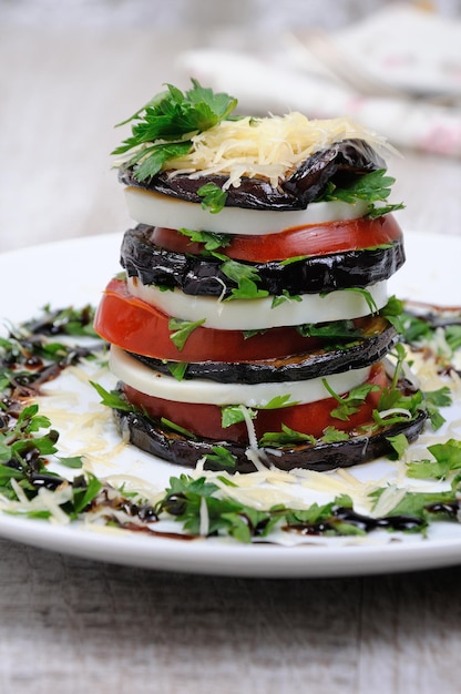 Apéritif de mozzarella d'aubergine dans une pile avec des tomates renversées avec du parmesan assaisonné d'herbes