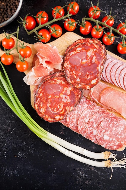 Apéritifs de viande à côté de tomates cerises sur planche de bois vintage foncé