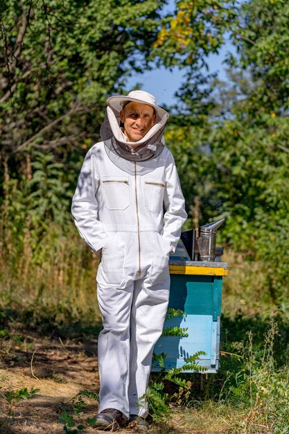 L'apiculteur pose devant la caméra en uniforme de protection dans une petite ferme apicole. Notion d'apiculture. Journée d'été au rucher.