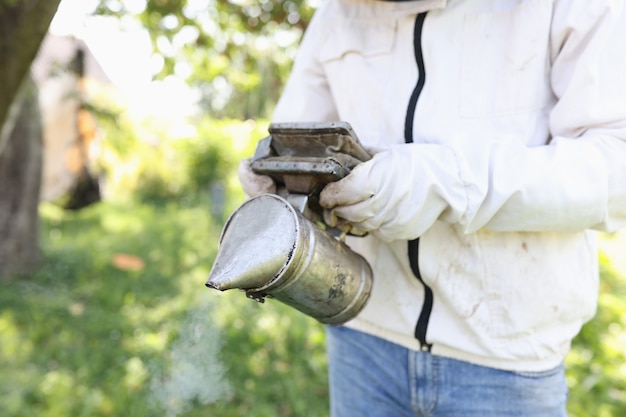 Apiculteur tenant un fumeur pour fumer des abeilles en gros plan concept d'apiculture de passe-temps