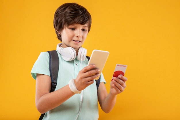 Appareil incroyable. Joyeux garçon aux cheveux noirs souriant et tenant son téléphone avancé