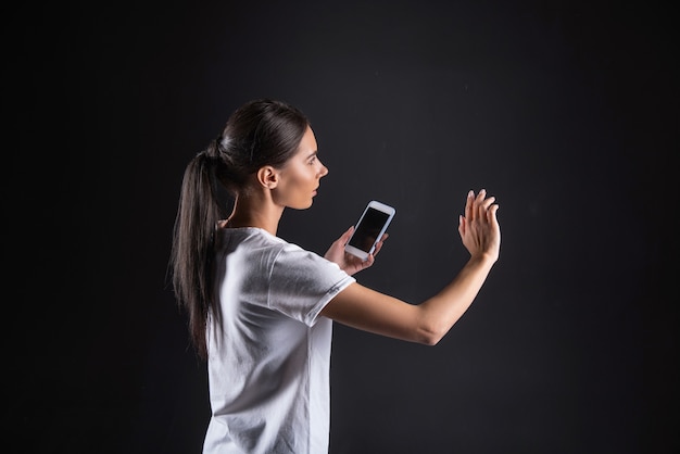 Appareil personnel. Belle jeune femme agréable tenant son téléphone portable et regardant l'écran sensoriel tout en utilisant les développements technologiques modernes