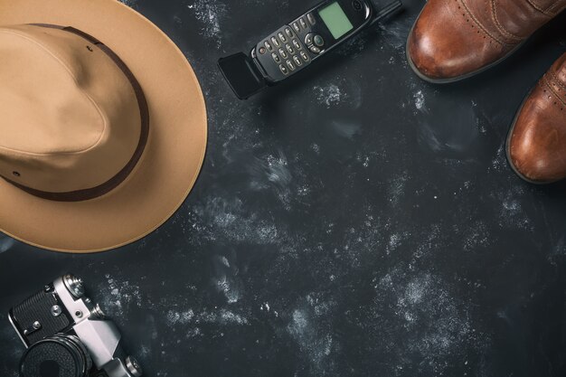 Appareil photo argentique vintage, chaussures marron, chapeau Fedora et vieux téléphone portable sur pierre noire