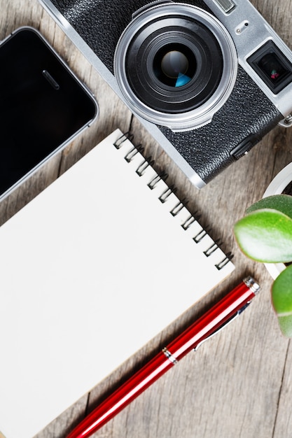 Appareil photo classique avec page vierge du bloc-notes et stylo rouge sur un bureau vintage en bois gris avec téléphone.