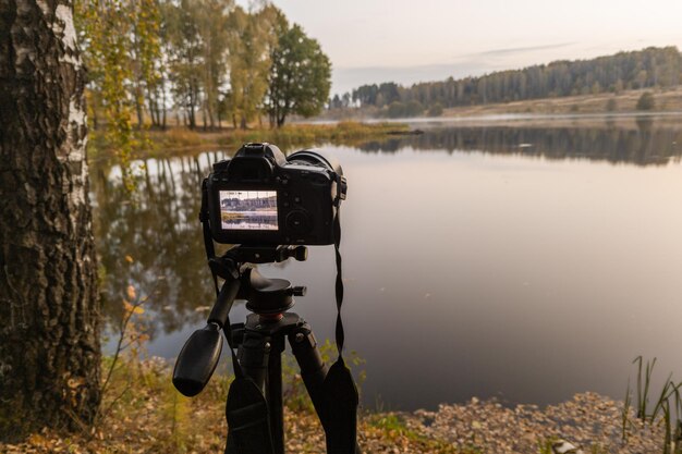 Appareil photo numérique noir sur trépied tirant tôt le paysage brumeux du matin au lac d'automne avec mise au point sélective